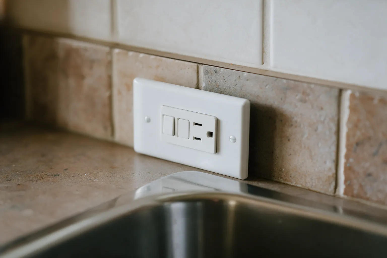 A GFCI receptacle with test and reset buttons in a kitchen backsplash beside the sink