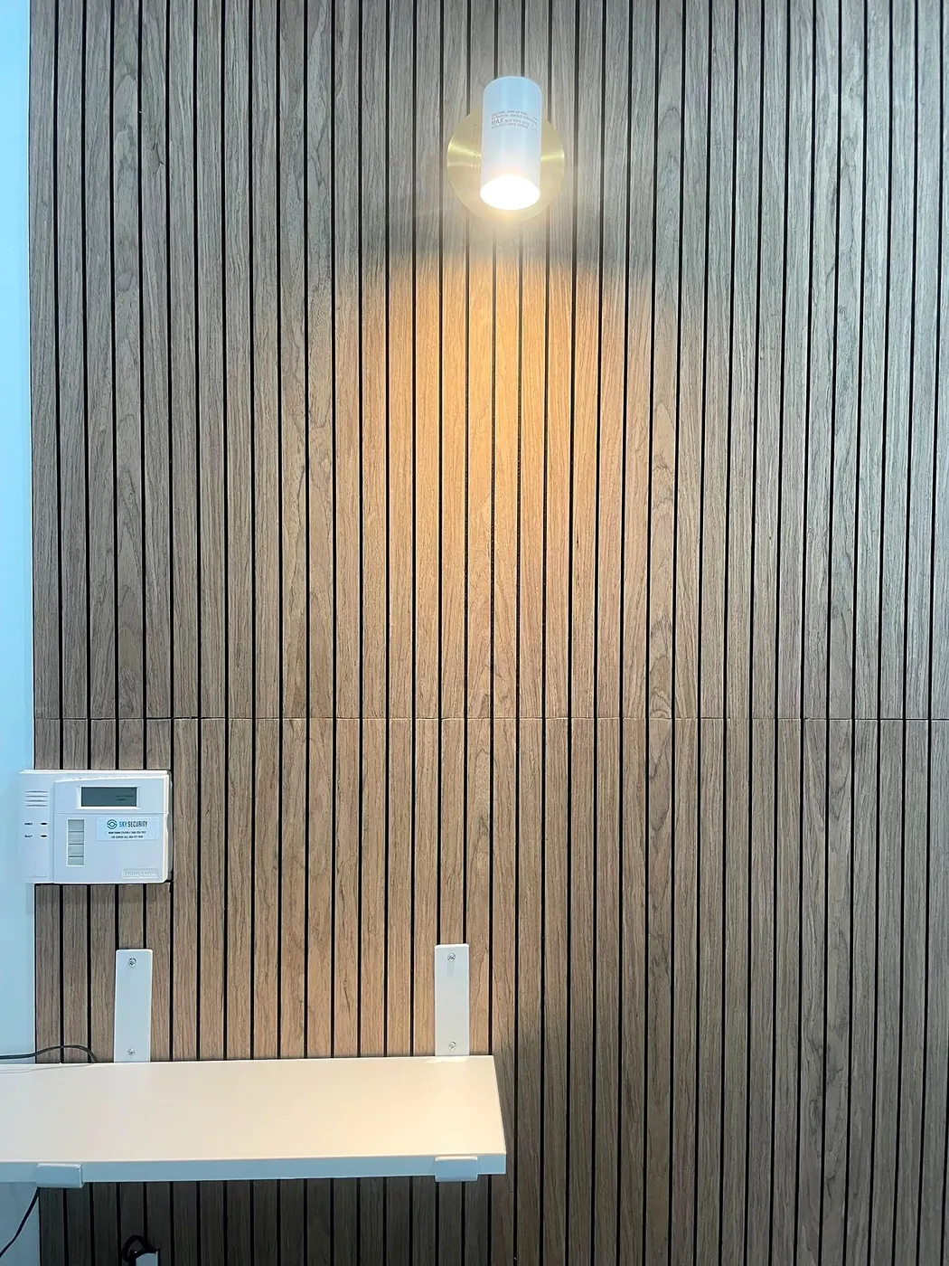 Surface-mounted downlight casting warm light down a wood slat feature wall above a white shelf