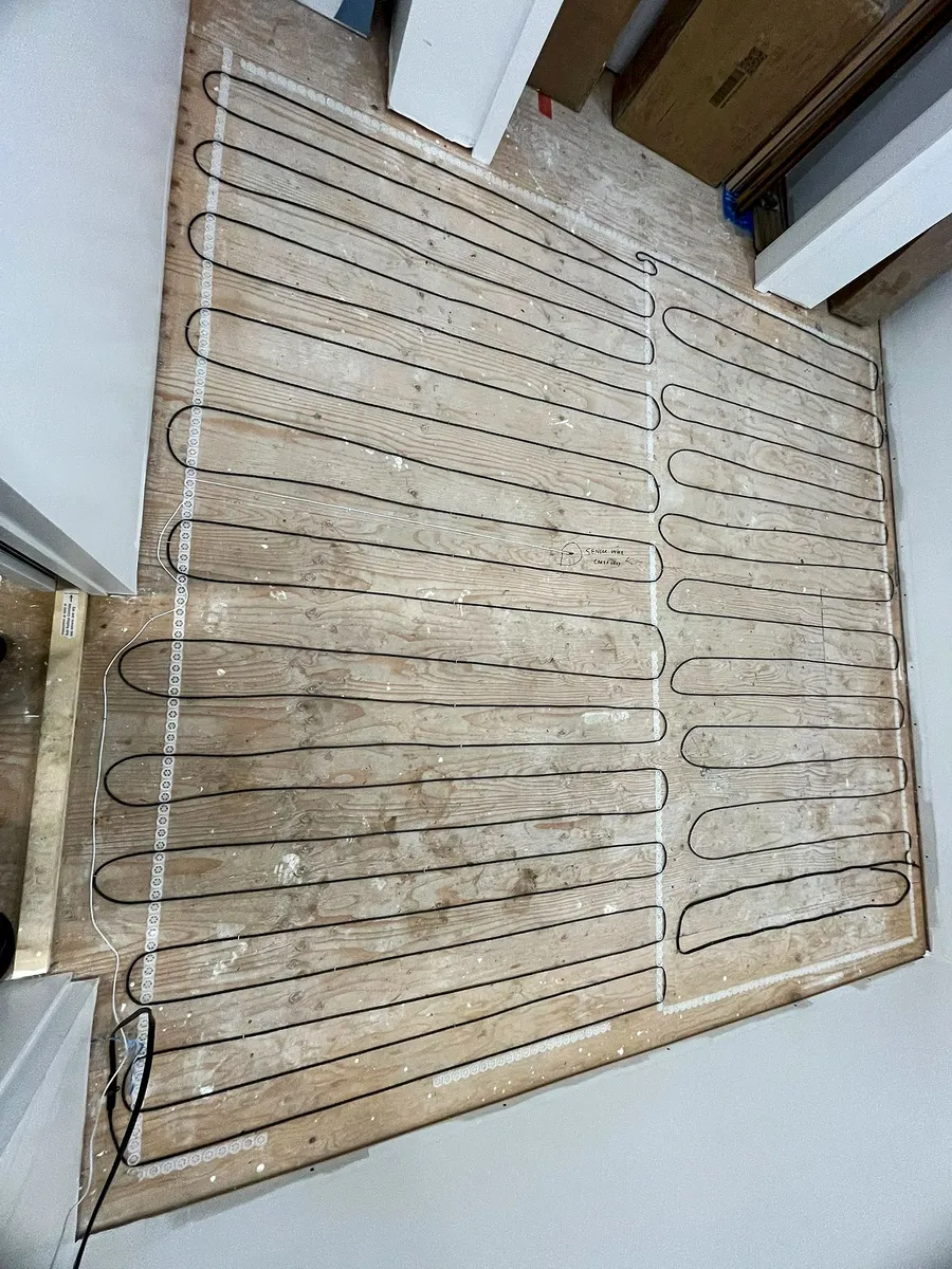 Electric floor heating cable looped in even rows across a plywood subfloor in Maple Ridge before tile