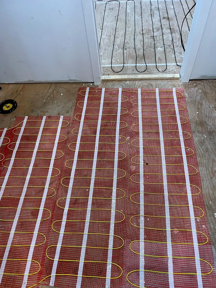Electric floor heating mats laid across a washroom subfloor in Maple Ridge, with the toilet flange and a heating cable run in the doorway