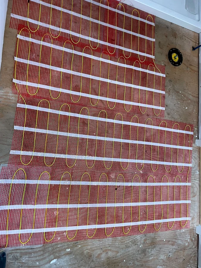 Orange floor heating mats with yellow heating cable laid edge to edge over a room subfloor, a floor box set at the side