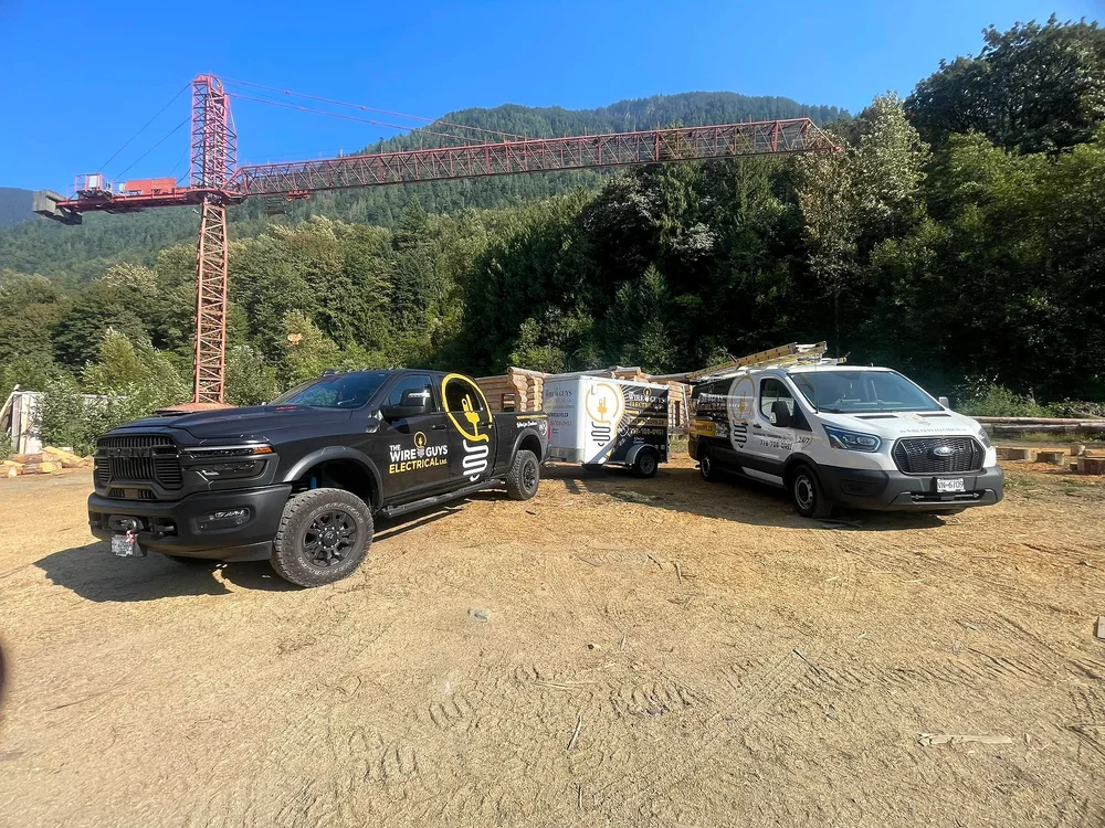The Wire Guys truck and van on a log-home build site with a tower crane and the mountains behind