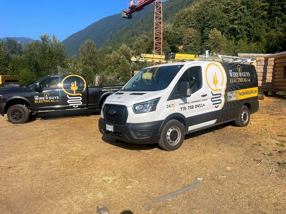 The Wire Guys van and pickup truck parked side by side on a log-home build site in the Harrison and Agassiz area