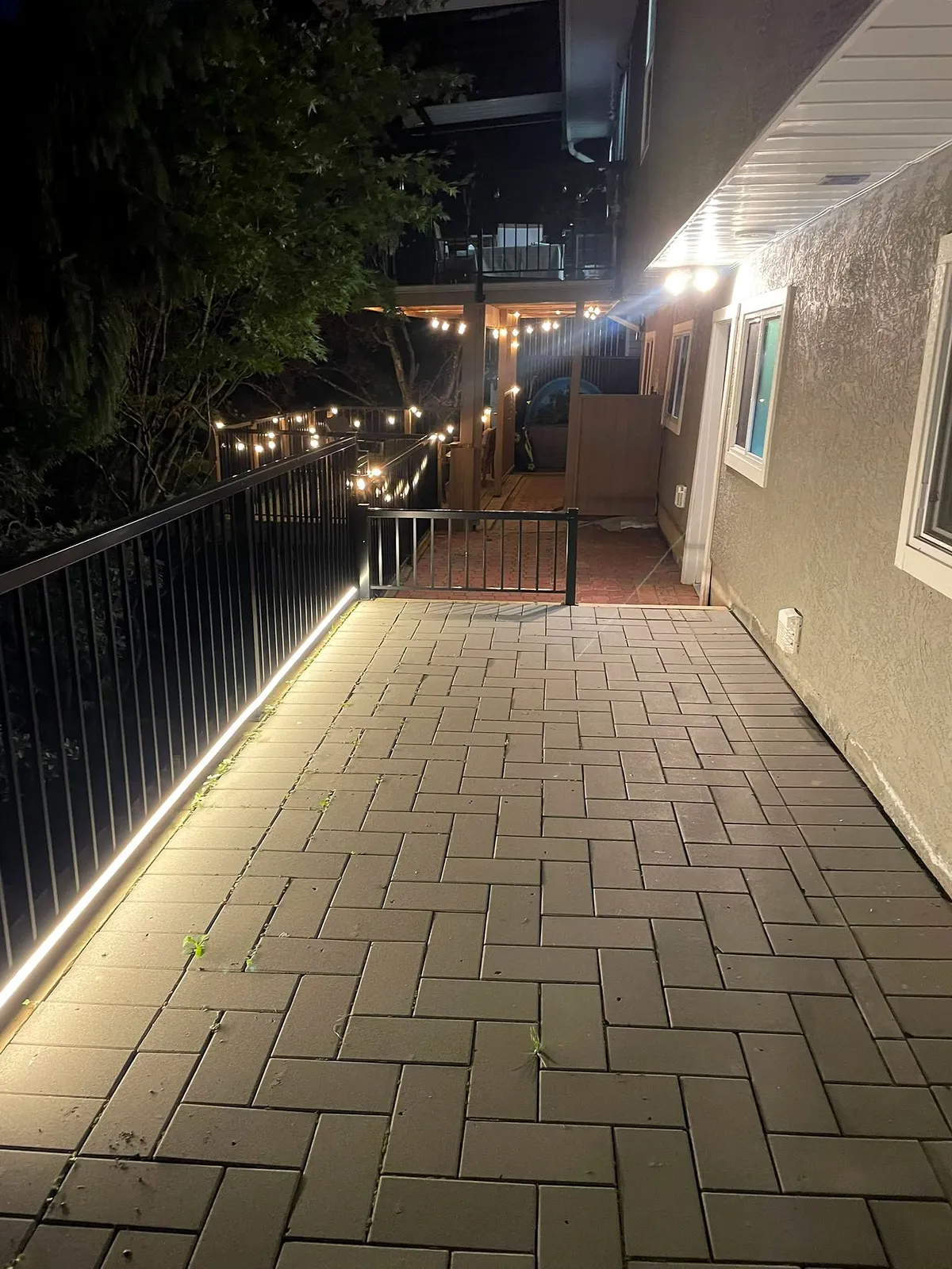 LED strip lighting under a black patio railing lighting a paver walkway at night