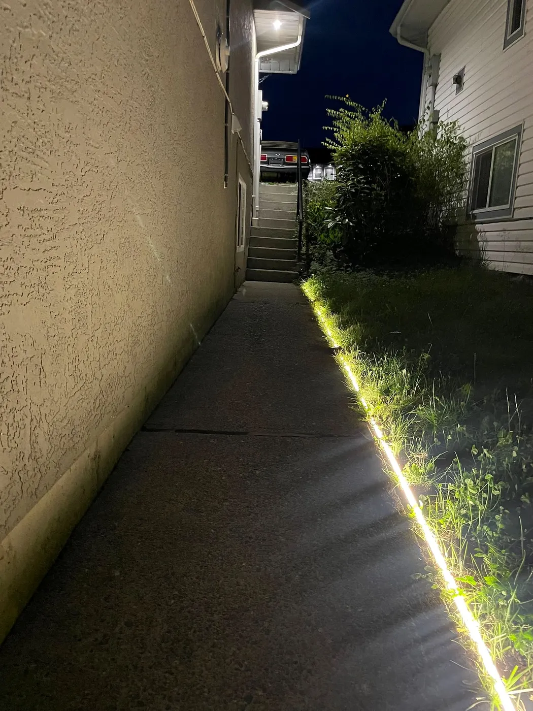 LED strip lighting along the edge of a concrete side path beside a house at night